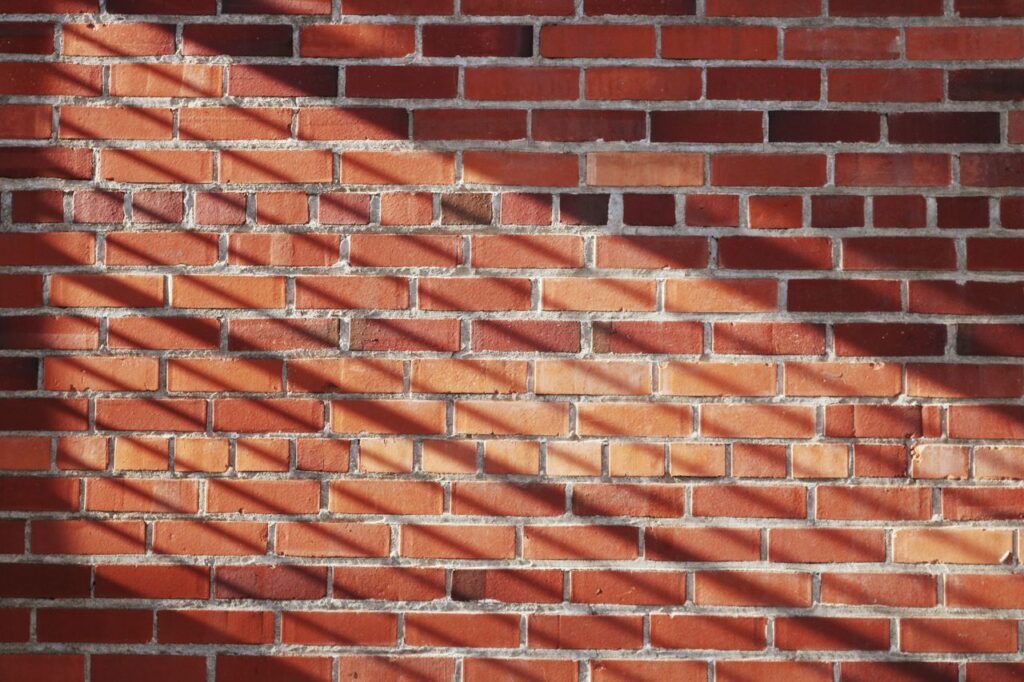 🧱 Premium Wallpapers Red brick wall with striking shadows creating a textured pattern.