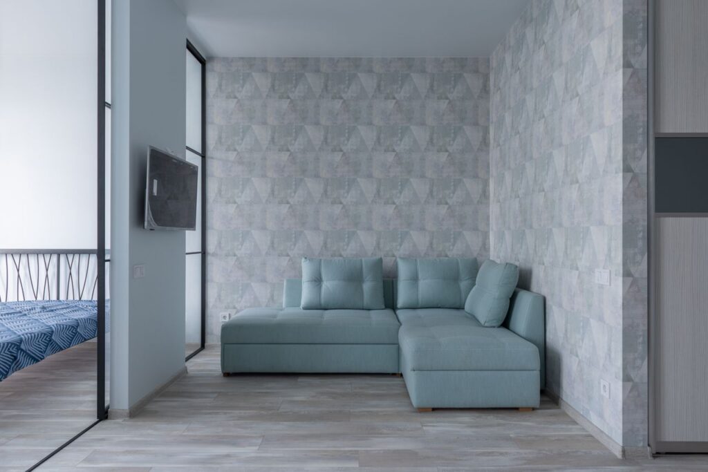 🧱 Premium Wallpapers Comfortable sofa with cushions placed near wall with wallpaper and bedroom with glass wall and bed in modern flat with TV
